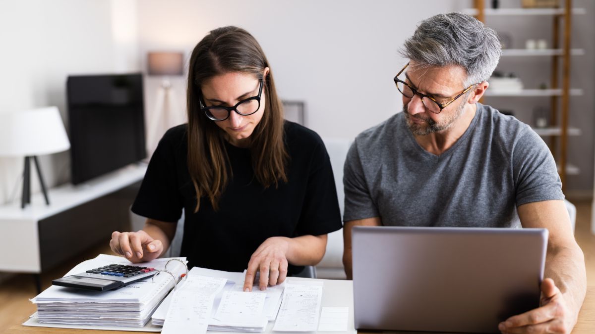 Uma mulher e um homem fazendo finanças com uma calculadora, um caderno e um laptop.